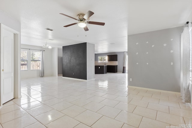 unfurnished living room with light tile patterned floors, baseboards, visible vents, and ceiling fan with notable chandelier