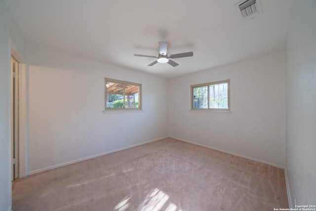 spare room featuring ceiling fan, light colored carpet, and a wealth of natural light