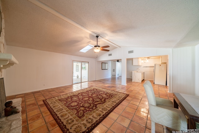 unfurnished living room featuring ceiling fan, vaulted ceiling with skylight, light tile patterned floors, and a textured ceiling