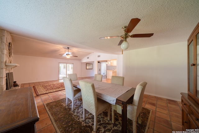 dining room featuring a textured ceiling, ceiling fan, light tile patterned floors, a stone fireplace, and lofted ceiling