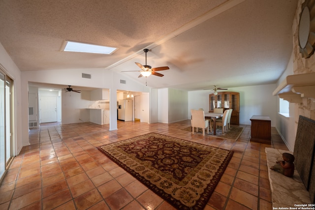 tiled living room featuring a textured ceiling, ceiling fan, and vaulted ceiling with skylight