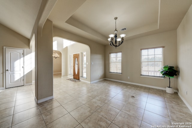 empty room featuring a raised ceiling, light tile patterned flooring, and a notable chandelier