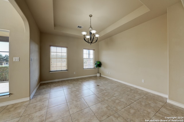 unfurnished room featuring a raised ceiling, light tile patterned floors, and a notable chandelier