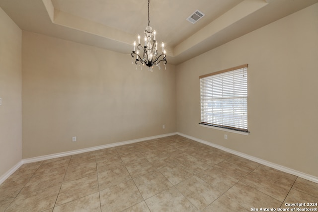 tiled spare room with a raised ceiling and a notable chandelier