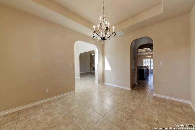 spare room featuring a notable chandelier, light tile patterned floors, and a tray ceiling