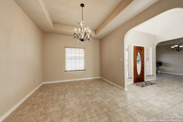 foyer with a tray ceiling, light tile patterned floors, and a notable chandelier