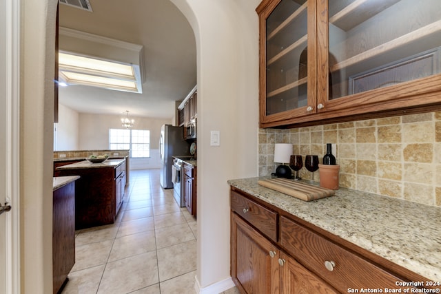 kitchen with tasteful backsplash, a notable chandelier, light tile patterned flooring, light stone counters, and stainless steel appliances