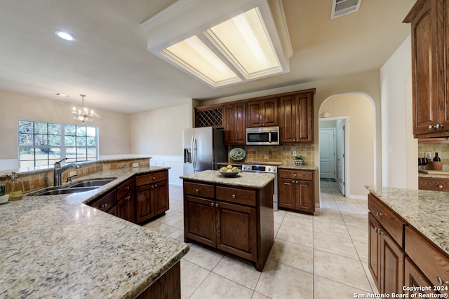 kitchen featuring a center island, sink, hanging light fixtures, stainless steel appliances, and light stone counters