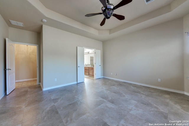 unfurnished bedroom featuring ceiling fan, ensuite bathroom, and a tray ceiling