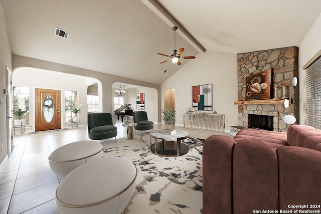 tiled living room featuring ceiling fan with notable chandelier, beam ceiling, a stone fireplace, and high vaulted ceiling