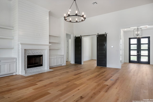 unfurnished living room with a chandelier, a barn door, light hardwood / wood-style floors, and french doors