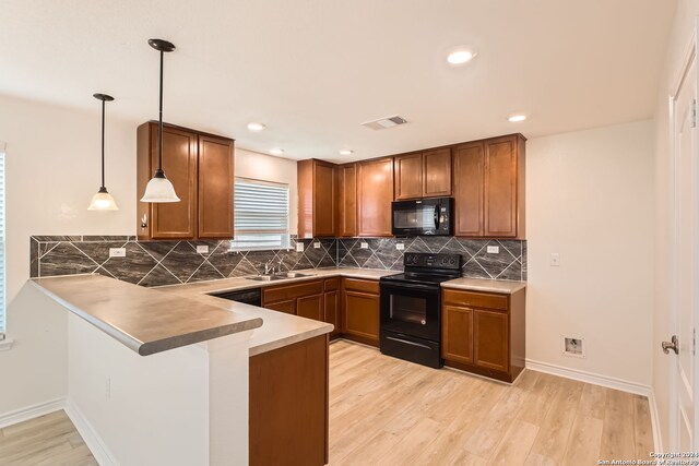 kitchen featuring black appliances, sink, light hardwood / wood-style flooring, decorative light fixtures, and kitchen peninsula