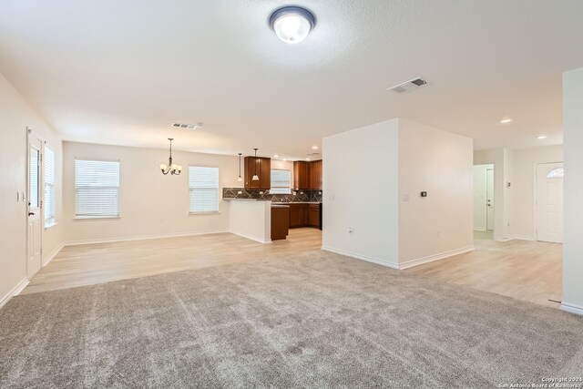 unfurnished living room featuring a chandelier and light colored carpet