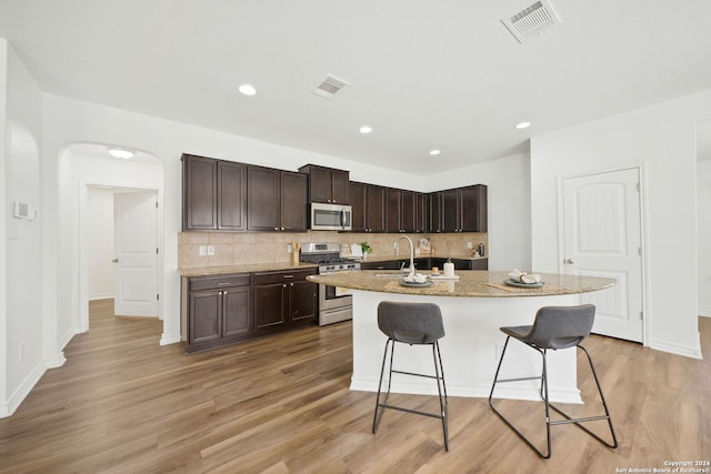 kitchen with a center island with sink, light hardwood / wood-style flooring, appliances with stainless steel finishes, a kitchen bar, and dark brown cabinetry