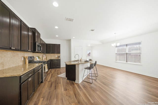 kitchen featuring dark brown cabinetry, dark wood-type flooring, an island with sink, decorative light fixtures, and appliances with stainless steel finishes