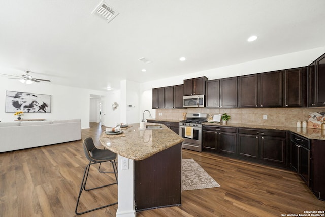 kitchen with appliances with stainless steel finishes, dark hardwood / wood-style floors, a breakfast bar area, and an island with sink