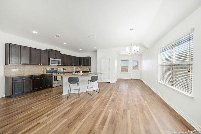 kitchen featuring dark brown cabinetry, stainless steel appliances, light hardwood / wood-style flooring, decorative light fixtures, and a breakfast bar