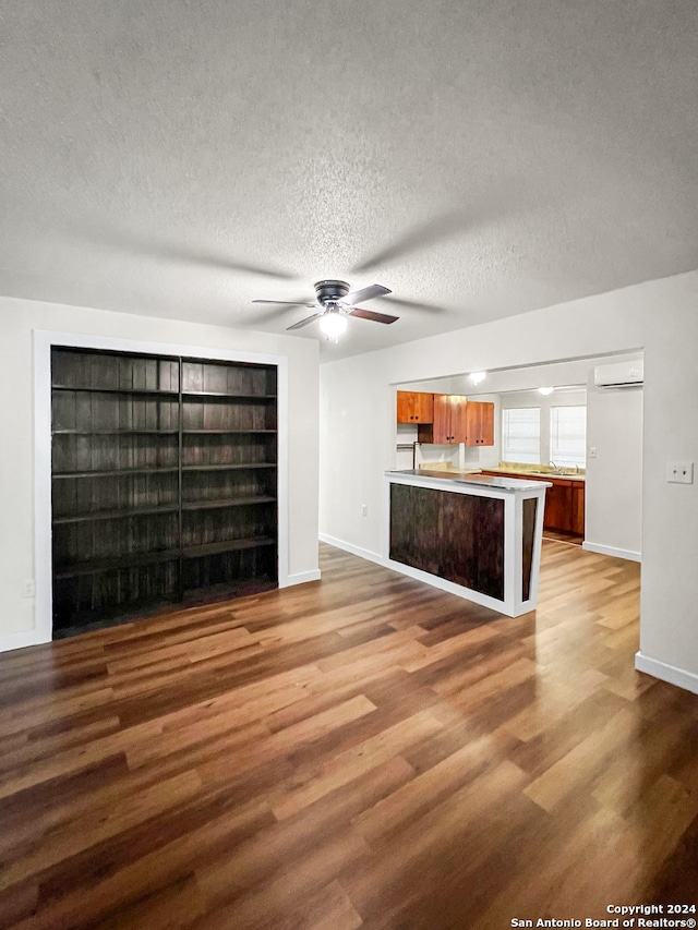 unfurnished living room with ceiling fan, wood-type flooring, a textured ceiling, and an AC wall unit