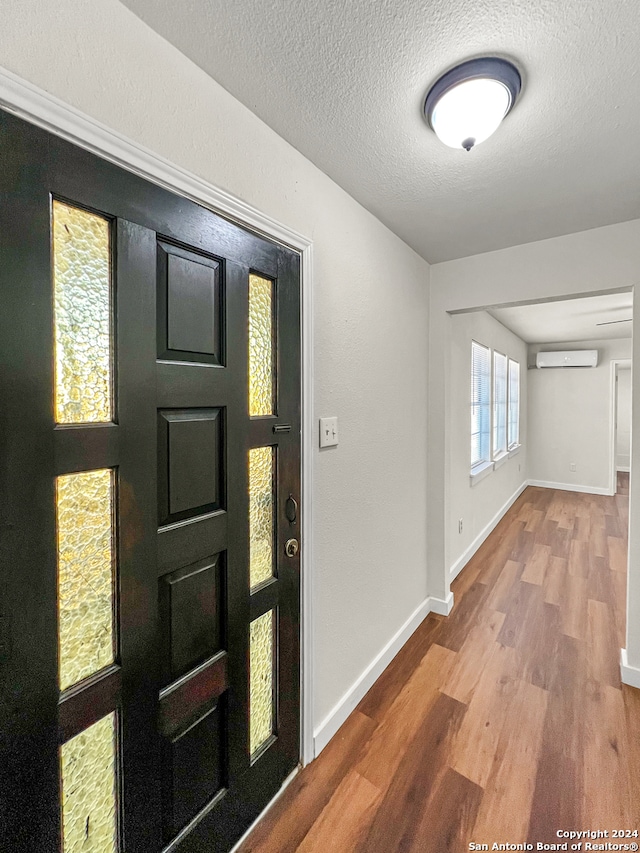 entryway with a wall mounted AC, hardwood / wood-style floors, and a textured ceiling