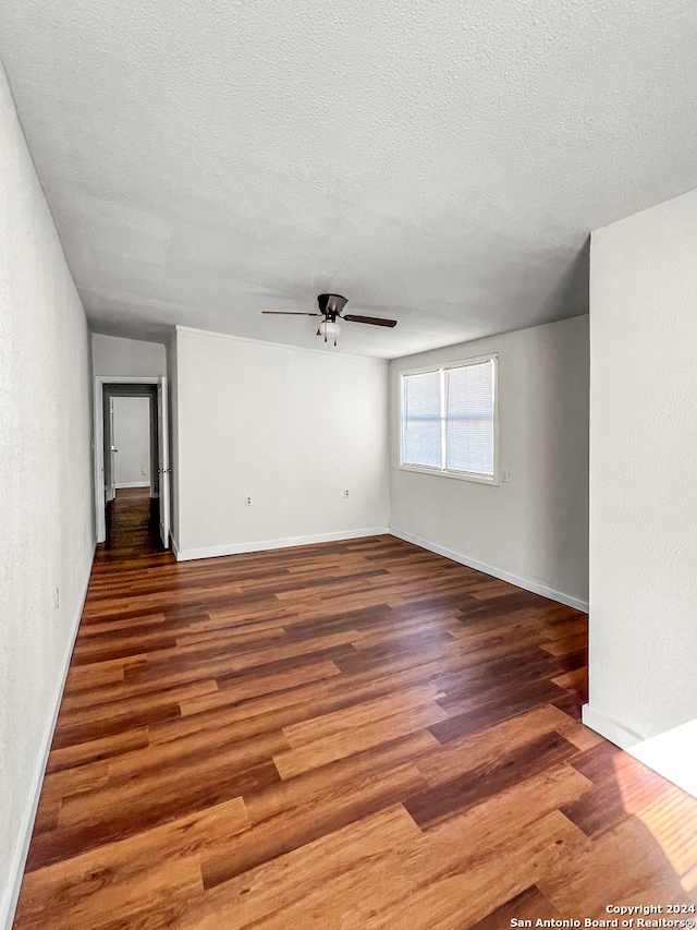 empty room featuring ceiling fan, dark wood-type flooring, and a textured ceiling