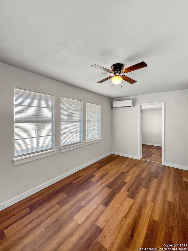 empty room with hardwood / wood-style floors, ceiling fan, a textured ceiling, and a wall unit AC