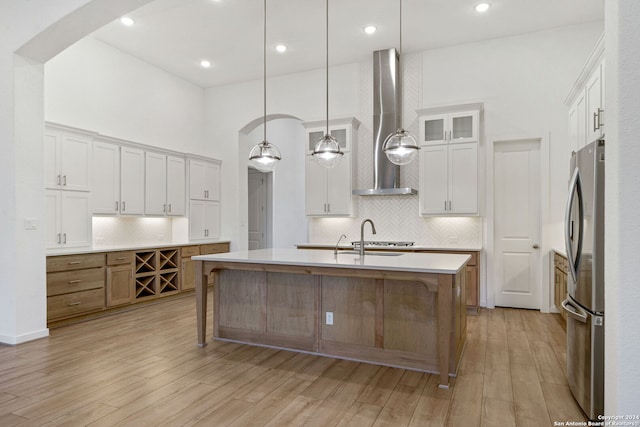 kitchen featuring wall chimney exhaust hood, light hardwood / wood-style floors, a center island with sink, white cabinets, and appliances with stainless steel finishes