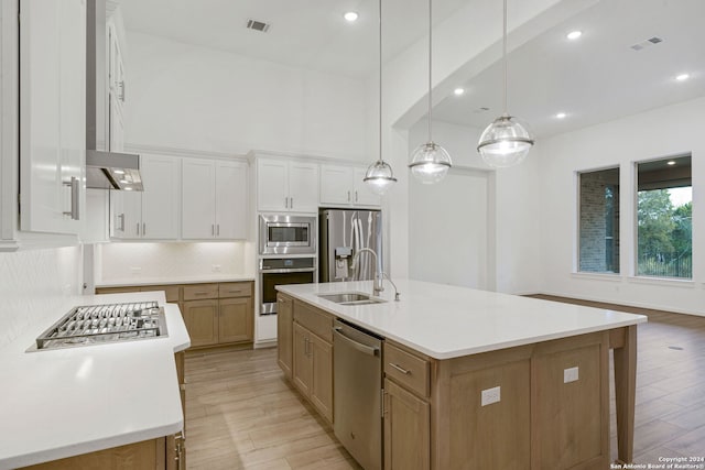 kitchen with appliances with stainless steel finishes, sink, decorative light fixtures, white cabinets, and an island with sink