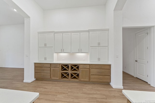 bar with tasteful backsplash, white cabinets, and light wood-type flooring