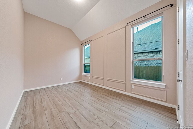 spare room featuring a textured ceiling, light wood-type flooring, vaulted ceiling, and plenty of natural light