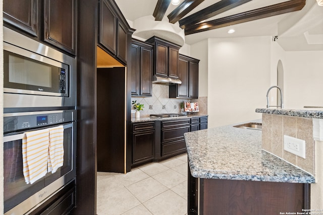 kitchen featuring light stone countertops, backsplash, dark brown cabinetry, stainless steel appliances, and sink