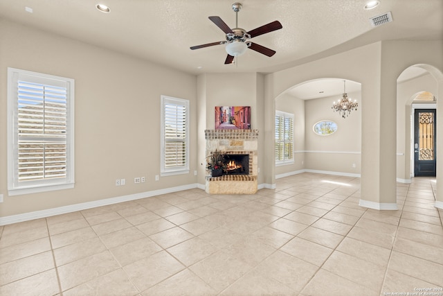 unfurnished living room with a textured ceiling, plenty of natural light, light tile patterned flooring, and ceiling fan with notable chandelier