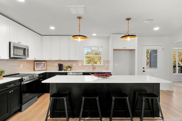 kitchen featuring a center island, stainless steel appliances, hanging light fixtures, and light hardwood / wood-style flooring