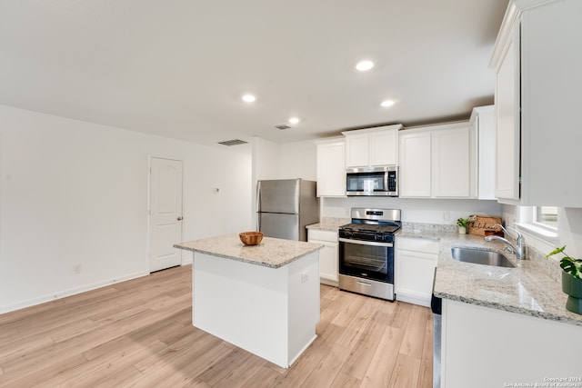 kitchen featuring light stone countertops, appliances with stainless steel finishes, a center island, light hardwood / wood-style floors, and white cabinetry