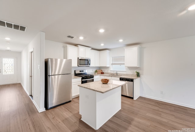 kitchen with white cabinets, a kitchen island, light wood-type flooring, and stainless steel appliances