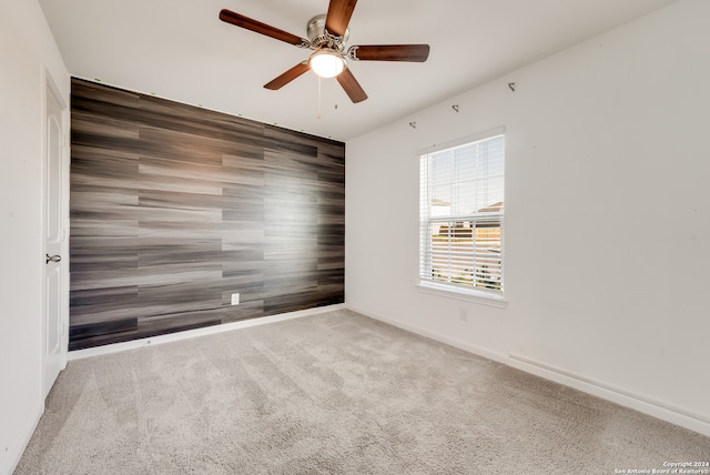 unfurnished room with carpet, wood walls, and ceiling fan