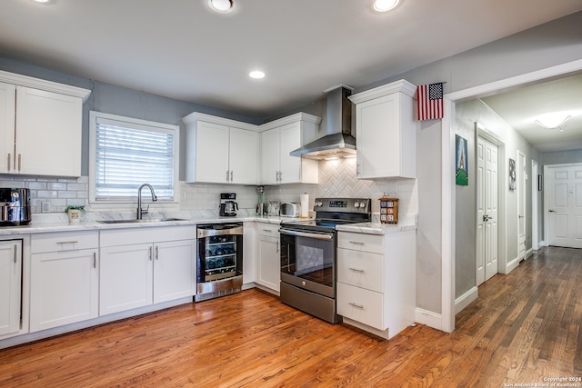 kitchen with stainless steel electric range oven, hardwood / wood-style floors, white cabinets, and wall chimney range hood