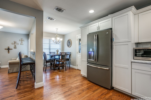 kitchen featuring white cabinetry, hanging light fixtures, stainless steel appliances, an inviting chandelier, and wood-type flooring