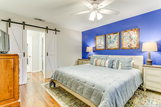 bedroom featuring light wood-type flooring, ceiling fan, and a barn door