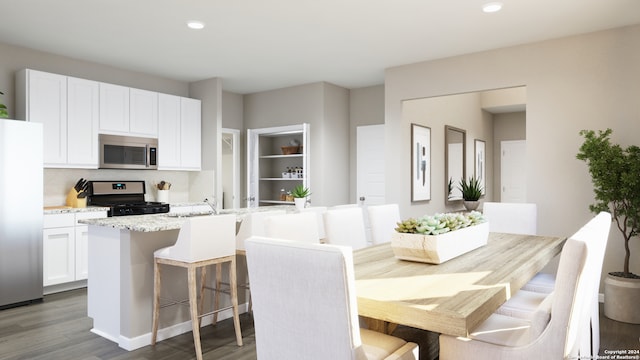 kitchen featuring hardwood / wood-style flooring, an island with sink, light stone counters, white cabinetry, and stainless steel appliances