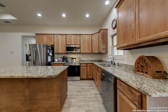 kitchen with appliances with stainless steel finishes, light wood-type flooring, light stone counters, and sink