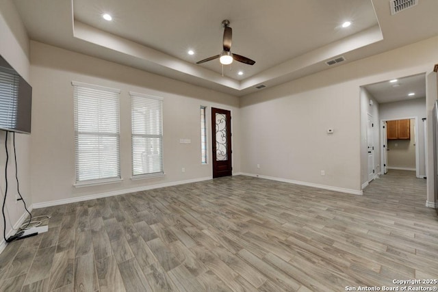 unfurnished living room featuring a tray ceiling and light hardwood / wood-style floors