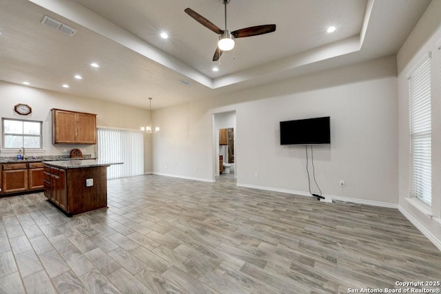 kitchen with pendant lighting, a center island, ceiling fan with notable chandelier, a tray ceiling, and light hardwood / wood-style floors