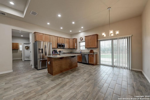 kitchen with pendant lighting, light stone countertops, a kitchen island, stainless steel appliances, and a chandelier