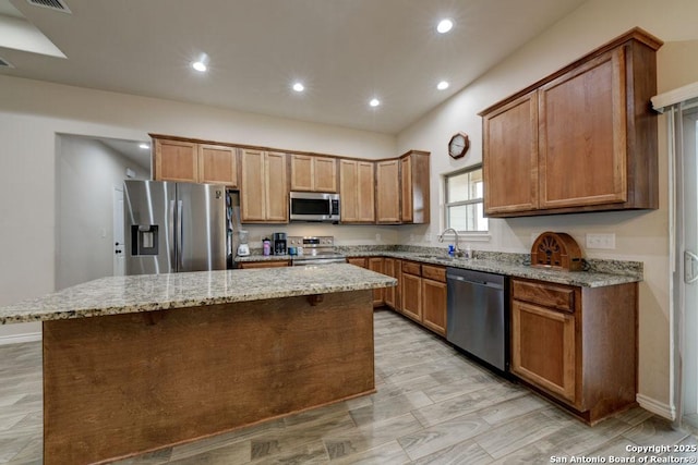 kitchen featuring a kitchen island, light stone counters, sink, and appliances with stainless steel finishes