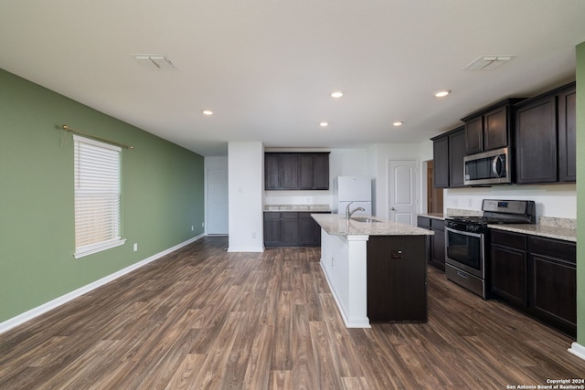 kitchen with sink, stainless steel appliances, light stone counters, dark hardwood / wood-style flooring, and an island with sink