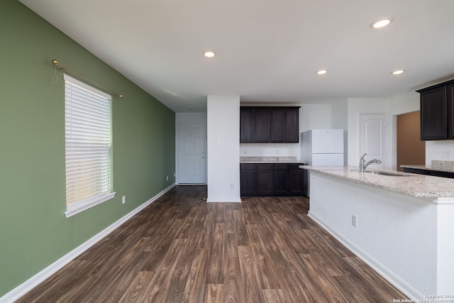 kitchen with sink, light stone counters, dark hardwood / wood-style flooring, white fridge, and a center island with sink