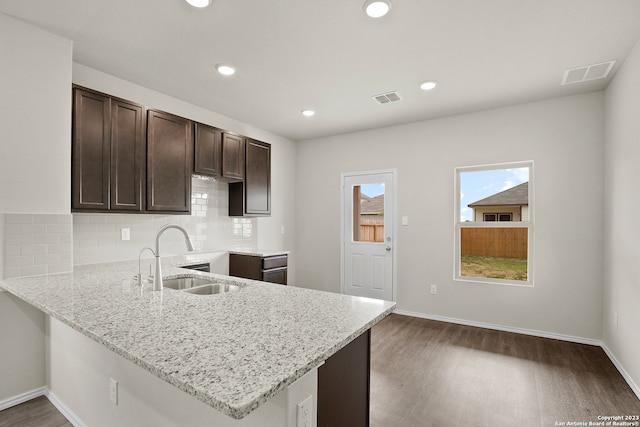 kitchen with light stone countertops, sink, dark wood-type flooring, kitchen peninsula, and decorative backsplash