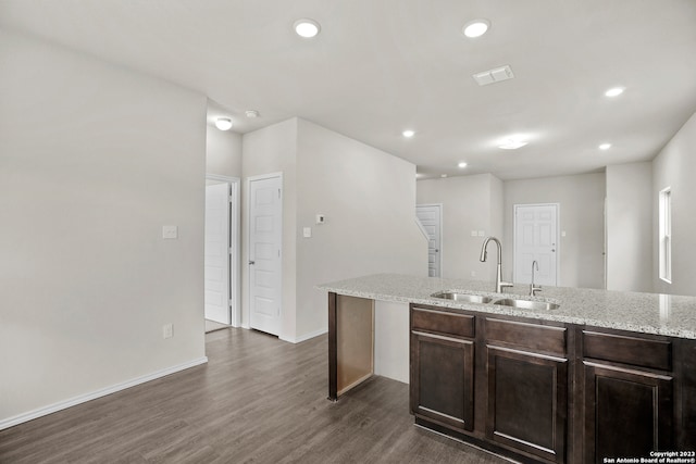 kitchen with sink, a center island, dark wood-type flooring, light stone counters, and dark brown cabinets