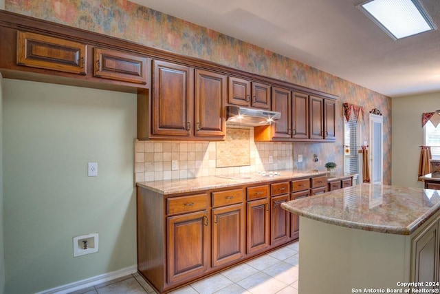 kitchen featuring light tile patterned flooring, white stovetop, tasteful backsplash, a center island, and light stone counters