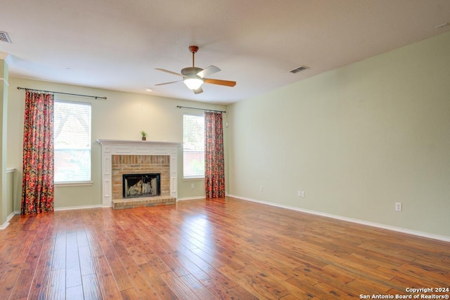 unfurnished living room featuring wood-type flooring, a brick fireplace, and a wealth of natural light